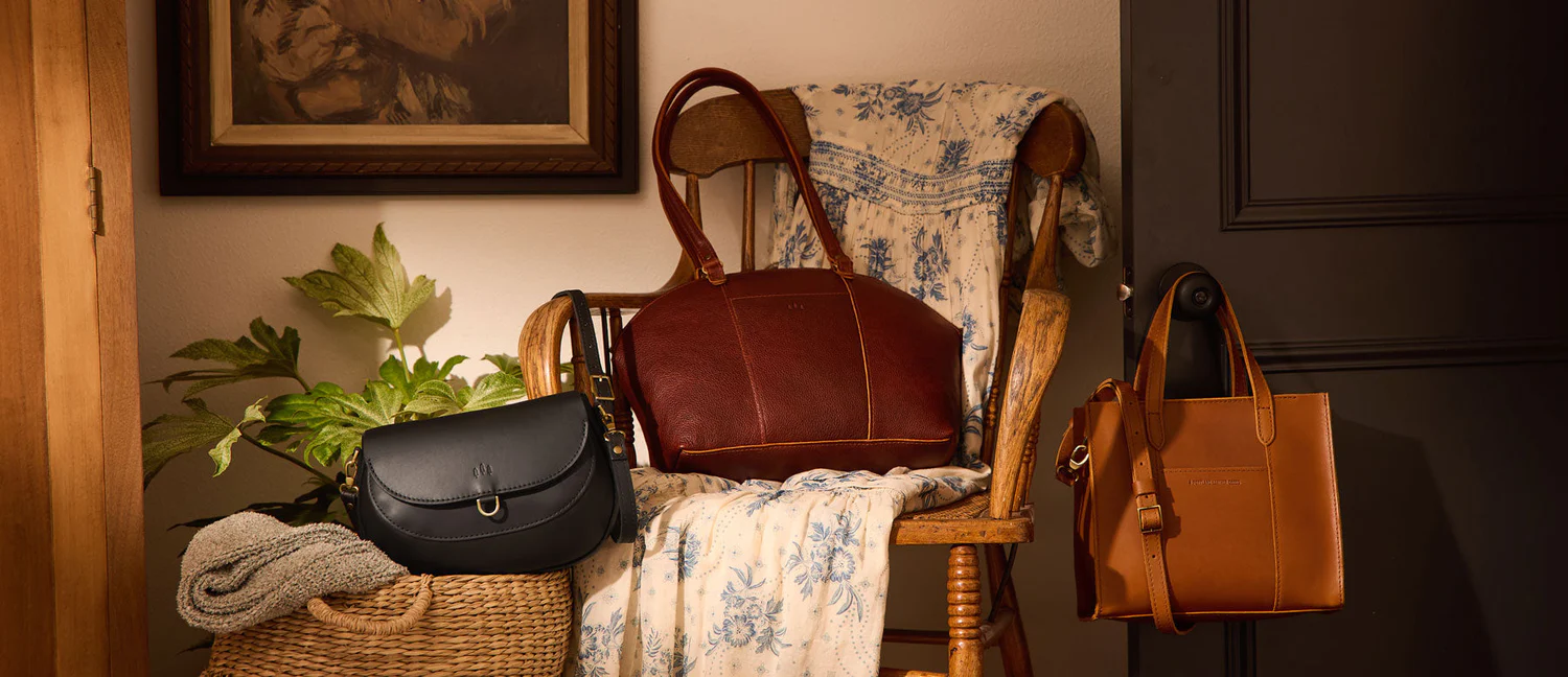 A row of handcrafted leather satchels in tan, black, grey and red on an atelier shelf